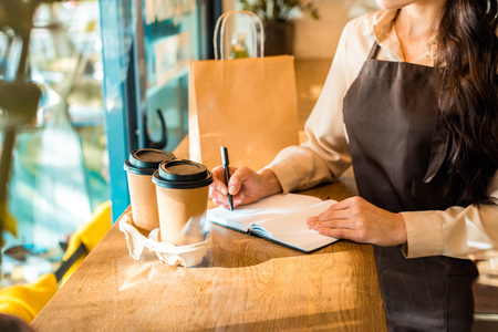 cropped image of waitress in apron writing something to notebook in cafeの写真素材
