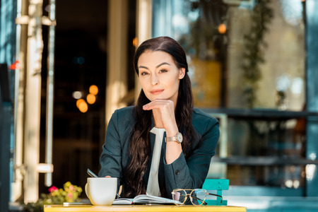 beautiful businesswoman resting chin on hand and looking at camera at street cafeの写真素材