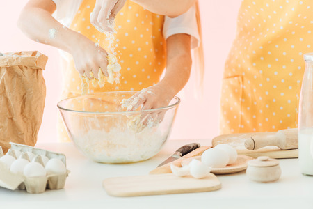 cropped shot of mother and daughter preparing dough in glass bowl together isolated on pinkの写真素材