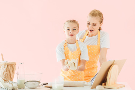 surprised young mother looking at daughter kneading dough isolated on pinkの写真素材