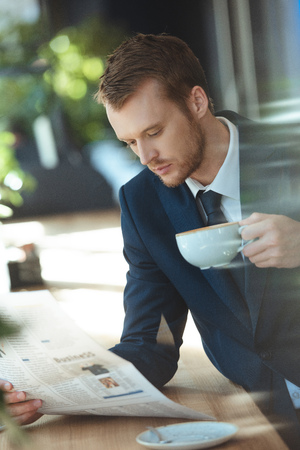 Businessman with cup of coffee reading newspaper during coffee break in cafeの写真素材