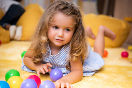 Adorable Caucasian kid lying on carpet with colored balls and looking away in kindergartenの写真素材