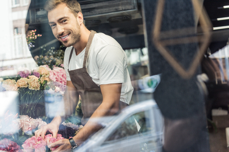 View through window of handsome florist taking care of flowers in flower shopの写真素材