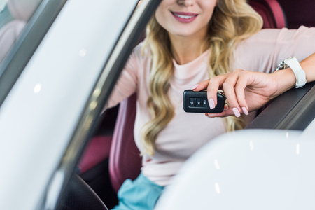 Partial view of woman with car key in hand sitting in new car in dealership salonの写真素材