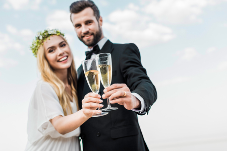 Selective focus of wedding couple clinking with glasses of champagne on beachの写真素材