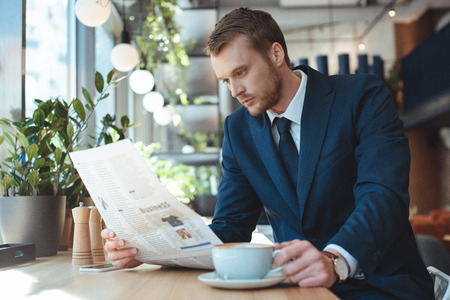 Businessman with cup of coffee reading newspaper during coffee break in cafeの写真素材