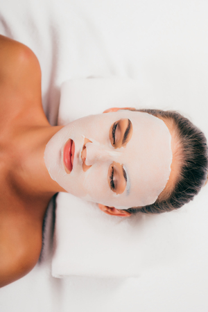 Attractive young woman in mask on face relaxing with closed eyes in spa centerの写真素材