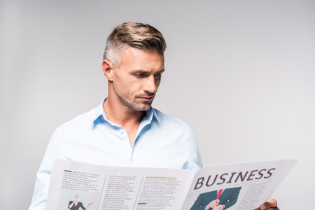 Serious adult businessman reading business newspaper isolated on white backgroundの写真素材