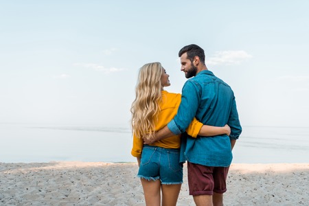 Back view of couple hugging, walking and looking at each other on beachの写真素材