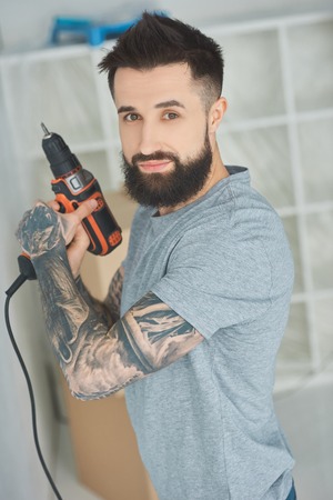 Portrait of tattooed man with screw gun in hands in new apartmentの写真素材