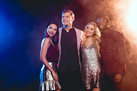 Beautiful smiling multiethnic friends hugging on party with smokeの写真素材