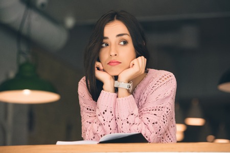 Selective focus of upset young woman sitting with book at table in cafeの写真素材