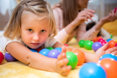 Adorable child lying on floor with colored toys and looking at camera in kindergartenの写真素材