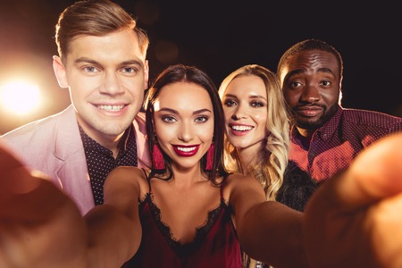 Happy glamorous multicultural friends taking selfieの写真素材