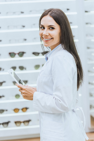 Smiling optician using digital tablet at work in ophthalmic shopの写真素材