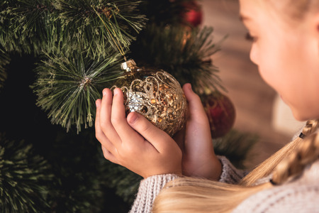 Cropped image of adorable preteen kid holding golden bauble in hands at homeの写真素材