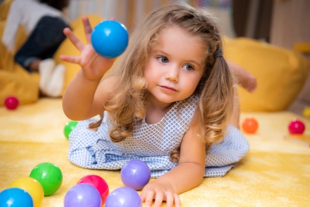 Adorable Caucasian kid playing on carpet with colored balls in kindergartenの写真素材