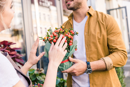 Cropped image of florist describing potted plant with red berries to customer near flower shopの写真素材