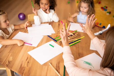 Educator showing number seven with fingers to multicultural kids in kindergartenの写真素材