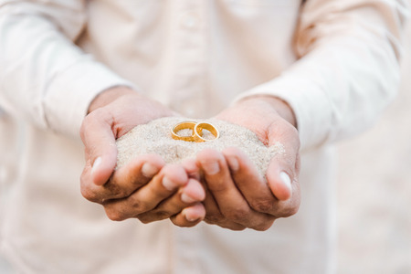 Cropped image of groom holding wedding golden rings with sand in hands on beachの写真素材
