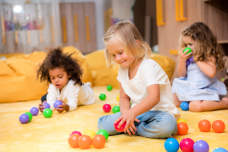 Adorable multicultural kids playing with colored balls on floor in kindergartenの写真素材