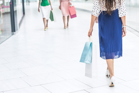 Low section of stylish girls in skirts and high heeled shoes walking with shopping bags in mallの写真素材
