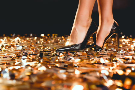 Cropped view of girl in black high heel shoes standing on golden confettiの写真素材