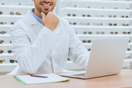 Cropped view of optician using laptop at table with papers in ophthalmic shopの写真素材