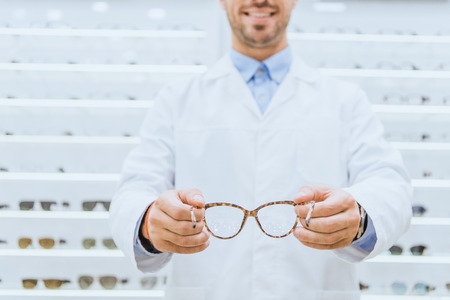 Cropped view of oculist in white coat holding eyeglasses, selective focusの写真素材