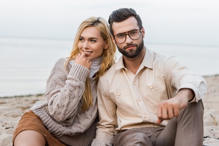 Attractive girlfriend and handsome boyfriend in autumn outfit sitting on sandy beachの写真素材