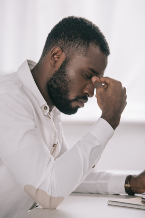Side view of tired African American businessman touching nose bridge in officeの写真素材