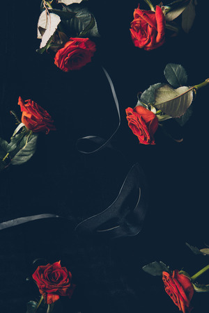 top view of black mask and beautiful red roses on blackの写真素材