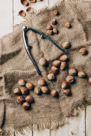 top view of tasty hazelnuts and nutcracker on sackcloth on wooden tableの写真素材