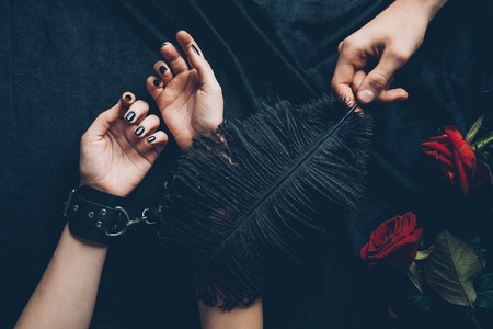 cropped shot of man holding black feather and woman in leather handcuffsの写真素材