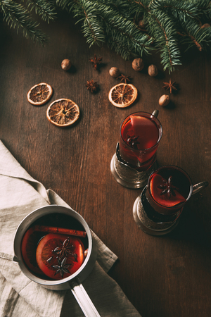 mulled wine in saucepan and glass cups on wooden background with dried orange slices and spicesの写真素材