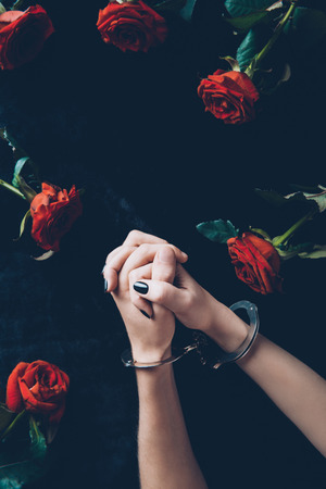 cropped shot of woman in handcuffs above black fabric with red rosesの写真素材
