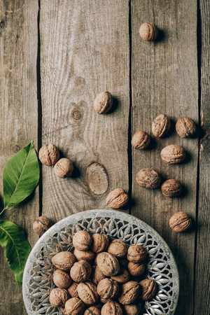 top view of ripe organic walnuts, green leaves and plate on wooden tableの写真素材