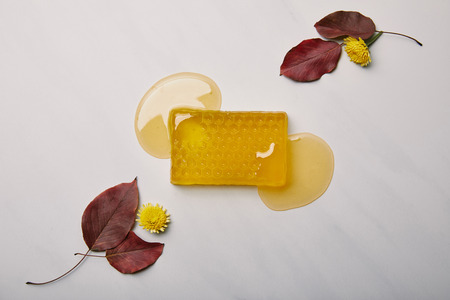 top view of handmade soap in shape of honeycomb with dandelions and leaves on white marble surfaceの写真素材