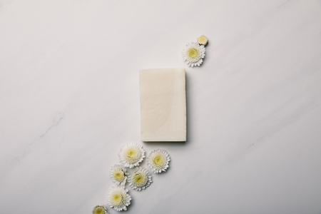 top view of white soap piece with daisies on white marble surfaceの写真素材