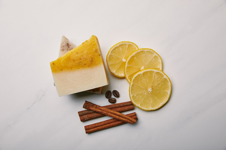 top view of handmade soap with lemon slices, cinnamon and coffee on white marble surfaceの写真素材