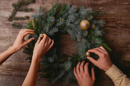 cropped image of girlfriend and boyfriend decorating christmas fir wreath together at wooden tableの写真素材