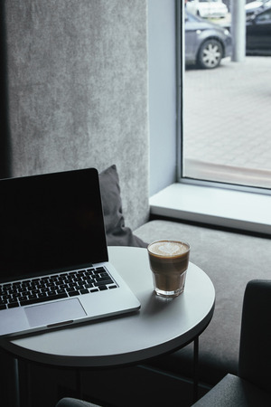 laptop with black screen and cup of coffee on table in cafeの写真素材
