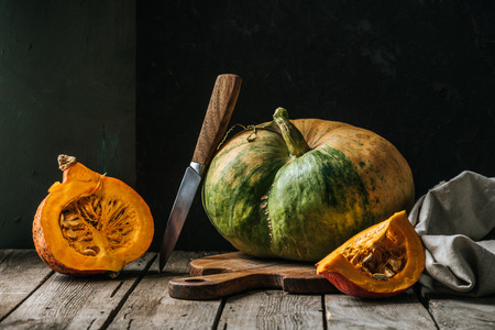 close up view of food composition with pumpkins, knife and cutting board on wooden surface on dark backgroundの写真素材