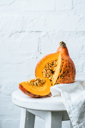 close up view of ripe cut pumpkin and linen on chair on white brick wall backdropの写真素材