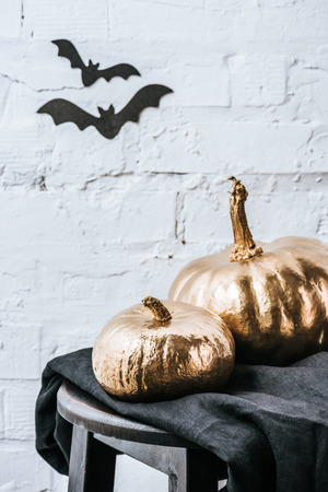 halloweenclose-up shot of two halloween pumpkins painted in golden metallic in front of white brick wall with bat stickersの写真素材