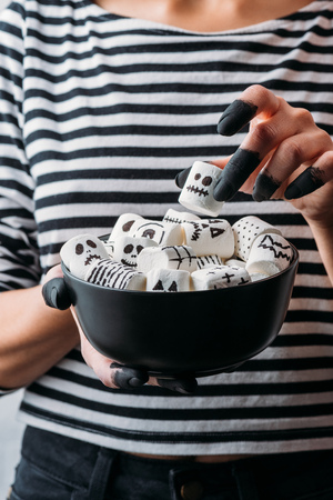cropped shot of woman holding bowl of marshmallows with skull faces, halloween conceptの写真素材