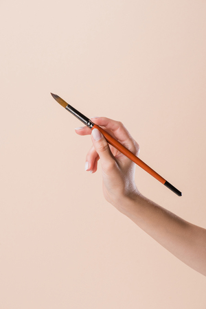 cropped shot of woman holding watercolor paint brush isolated on beigeの写真素材