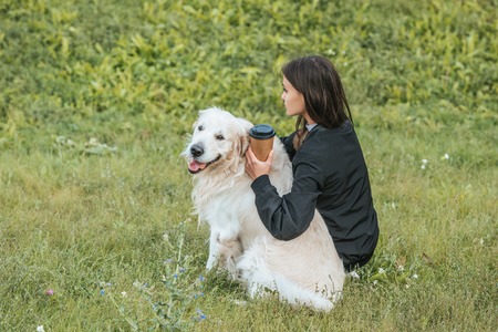 young woman holding paper cup and sitting with dog in parkの写真素材