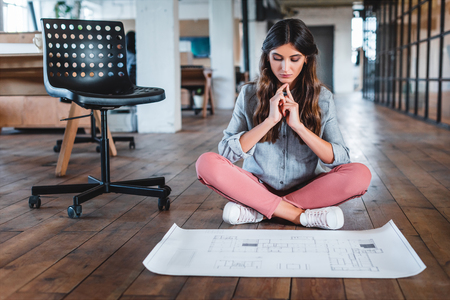 concentrated young businesswoman sitting in lotus position and working with papers in office