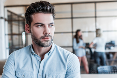 portrait of handsome pensive young businessman looking away in officeの写真素材